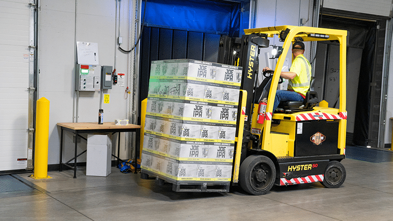 Worker operating a yellow forklift carrying boxes in a warehouse.